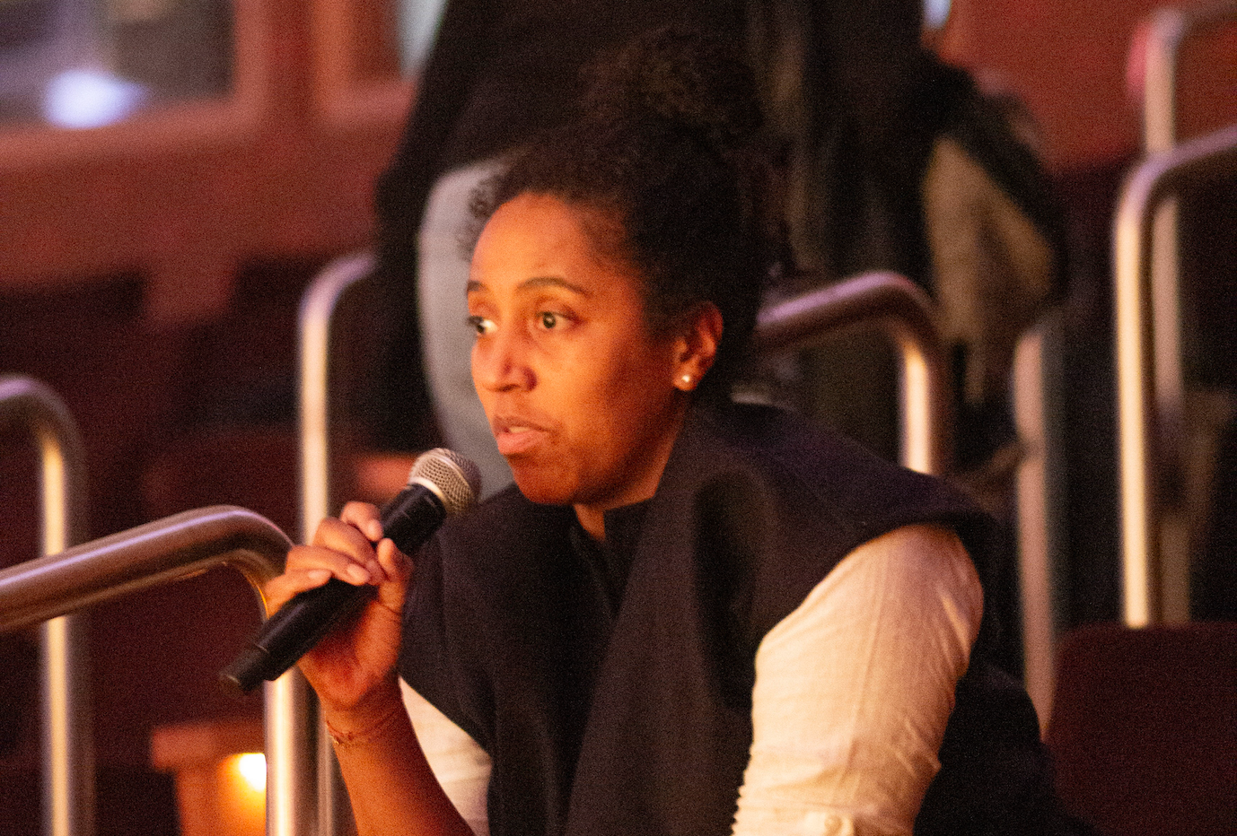 A middle-aged black woman, holding a microphone, asks Alice Diop a question during the Q+A portion of the event.